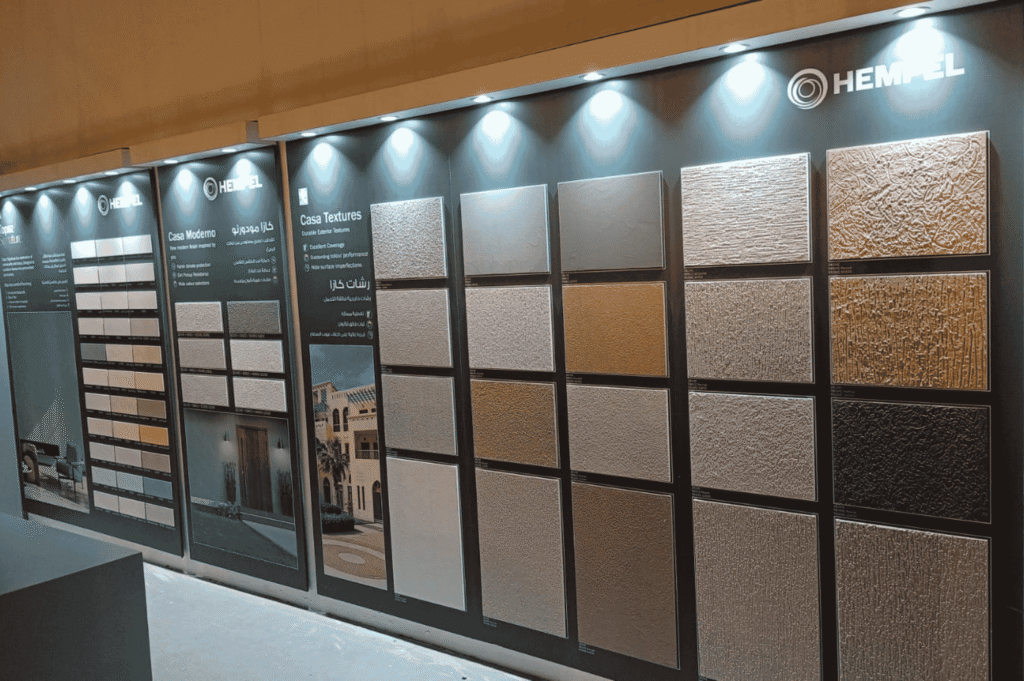 The interior of a Al-Khabeer paint store and showroom, showing a large wall display of color and texture samples for exterior paint and decorative coatings.